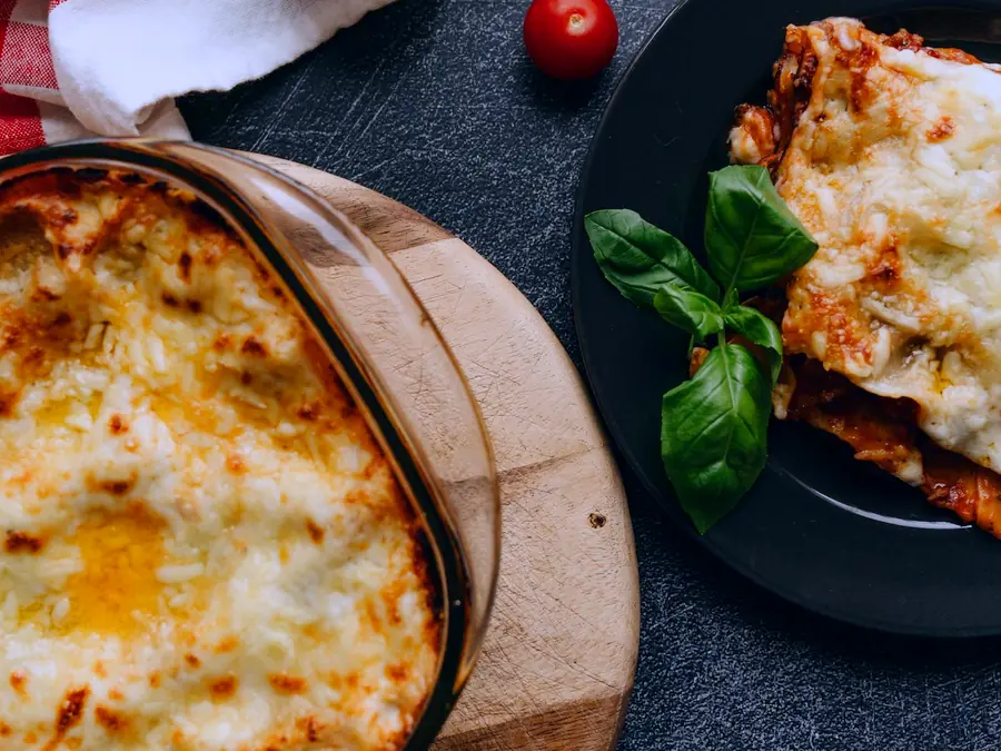 A dish of baked lasagna beside a plated slice with basil and cherry tomatoes